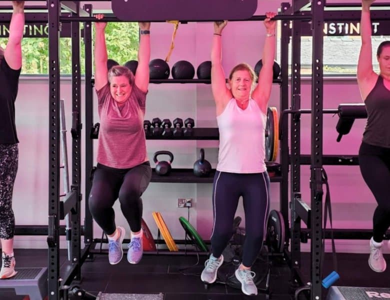 Four female clients, hanging from a bar in the main training area at Instinct Gym in Tarporley.